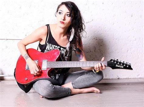 A Woman Sitting On The Floor With A Red Guitar In Her Hand And Looking At The Camera