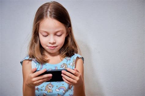 A Little Preschool Girl Plays Online Games On Her Smartphone And
