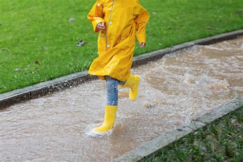 Cute Little Girl In Yellow Raincoat And Rubber Boots