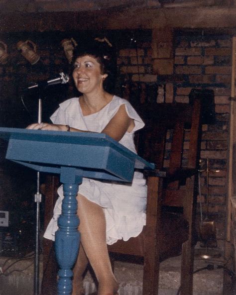 A Woman Sitting At A Blue Table With A Microphone In Her Hand And