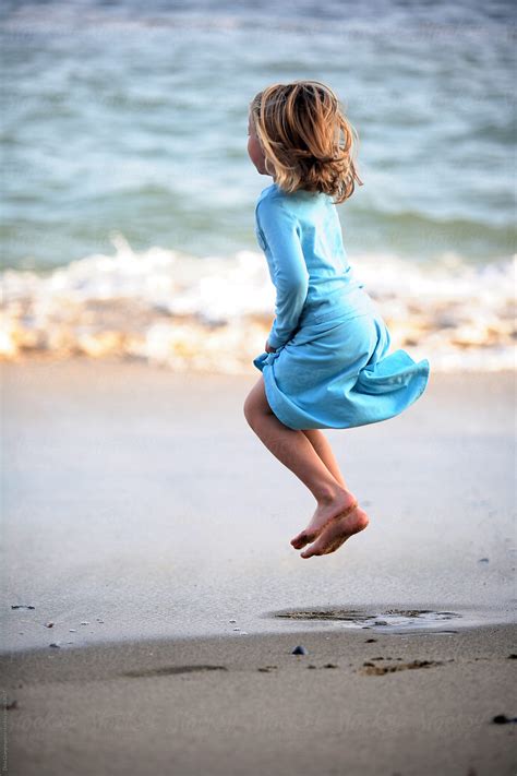Girl Jumping On The Beach Wearing Blue Dress By Dina Giangregorio Stocksy United