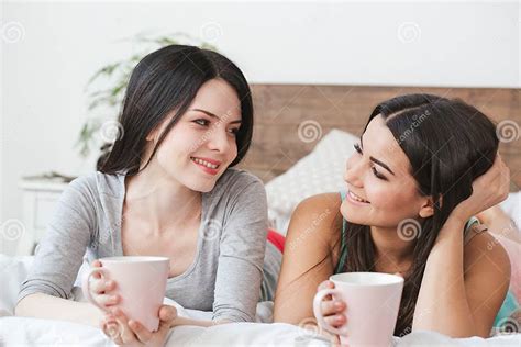 Lesbian Couple In Bedroom At Home Lying Drinking Tea Talking Playful