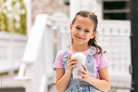 Young Girl Smiles To Camera While Enjoying A Milkshake By Stocksy