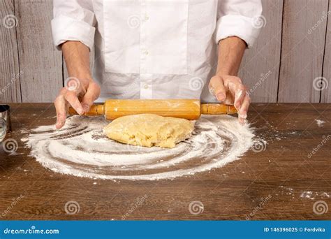 Hands Roll Out The Dough With A Rolling Pin On A Wooden Table In The