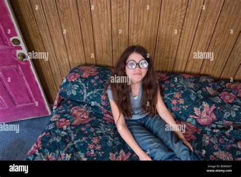Preteen Girl Wearing Funny Thick Glasses Sitting On A Bed In A Motel Room Model Released Stock