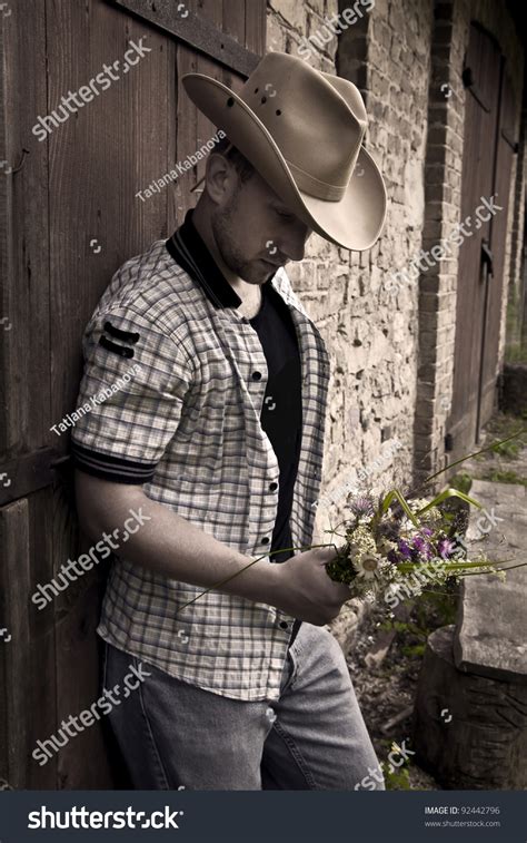 Young Handsome Sad Man In Cowboy Hat Standing With Bunch Of Flowers