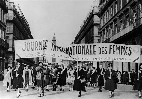 A Group Of Women Marching Down A City Street Holding Up A Sign That Reads Journal International