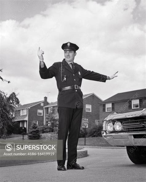 1960s single smiling uniformed policeman arms hands extended standing at intersection directing