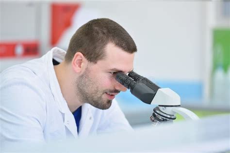 Young Male Scientist Looking Through A Microscope In A Laboratory Doing