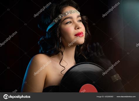 old fashioned woman dressed in style of art deco holding vinyl record on dark background