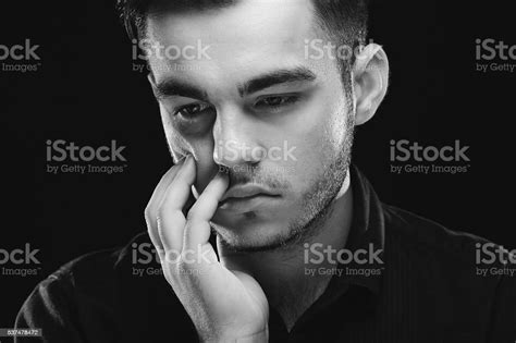 Sad Young Man Looking Down On Dark Studio Background Stock Photo