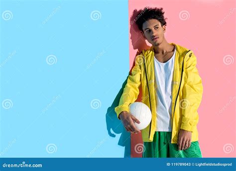 Handsome Young Man Holding Ball In Hand And Looking Away On Pink Stock