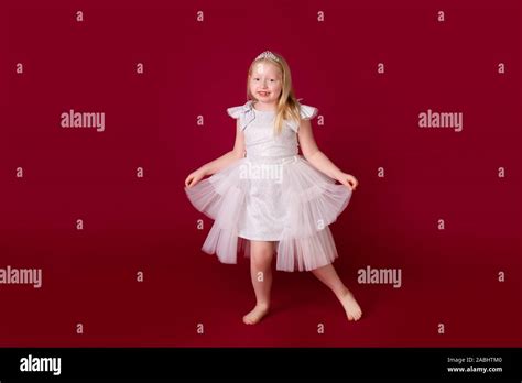 Beautiful Little Blonde Princess Dancing In Luxury White And Silver Dress Isolated On Red