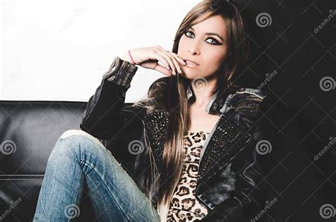brunette wearing denim jeans leopard top and leather jacket sitting in sofa posing seductively