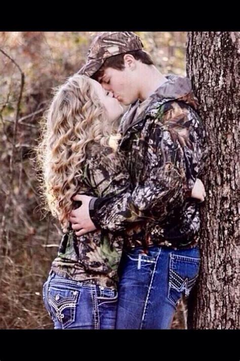 Two People Standing Next To Each Other Near A Tree In The Woods One Is Kissing The Other S Head