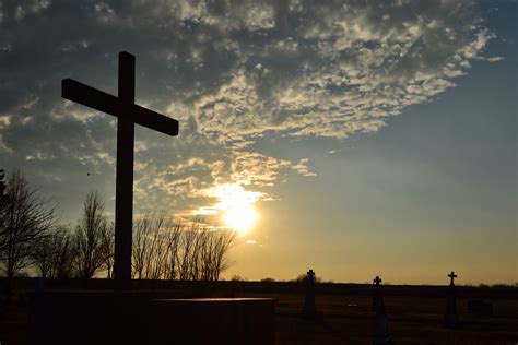 The Sun Is Setting Behind A Large Cross
