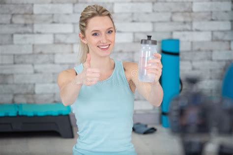 Happy Girl Drinking Water Bottle At Fitness Center Doing Thumbs Up