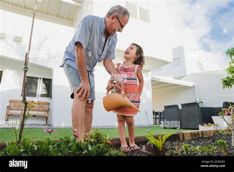 Smiling Grandfather And Grandbabe In Backyard Garden Together Holding Watering Can Have Fun