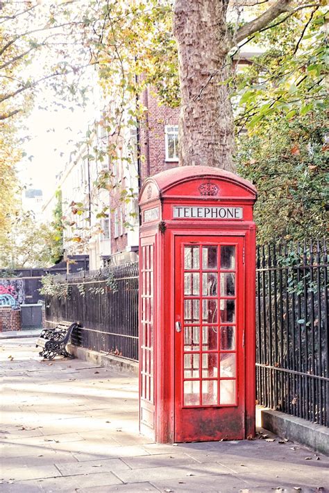 A Red Telephone Booth Sitting On The Side Of A Road Next To A Tree And