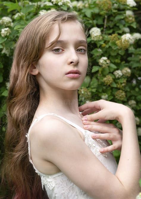 white beautiful girl 11 years old with long hair in a white dress near a birch tree on a green