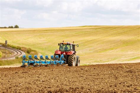 Farmer In A Big Red Tractor Preparing Land With Plow For Sowing Stock