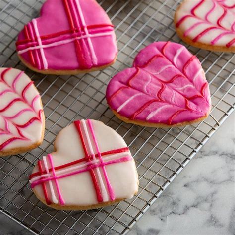 Four Decorated Heart Shaped Cookies Sitting On A Cooling Rack With Pink