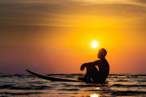 Silhouette Of Surf Man Sit On A Surfboard Surfing At Sunset Stock