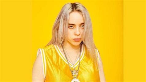 Billie Eilish Is Wearing Yellow Dress And Chains On Neck Standing In