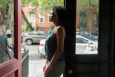 woman looking out front door of apartment to city street by stocksy contributor jamie grill