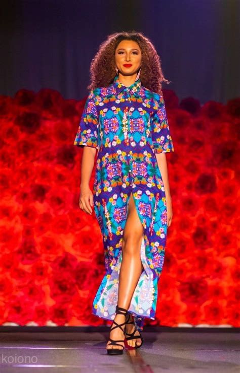 A Woman Walking Down A Runway Wearing A Colorful Dress With Flowers On