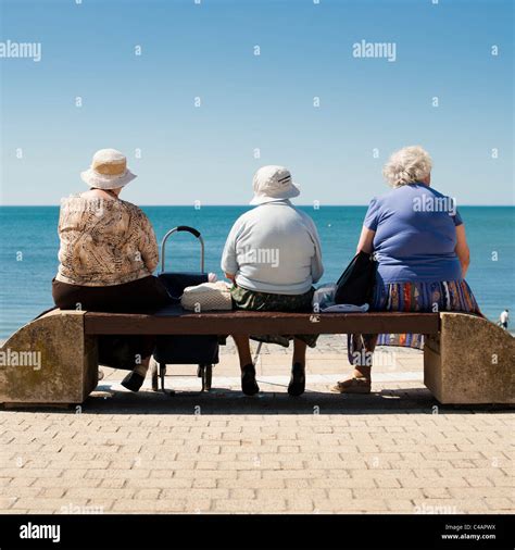 A Rear View Of Three Old Elderly Women Sitting On A Seaside Bench