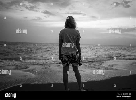 A Grayscale Shot Of A Girl Standing On The Sandy Coast Of An Ocean