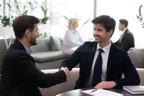 Smiling Businessmen In Suits Shaking Hands After Signing Agreement