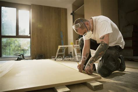 Construction Worker With Tattoos Measuring And Marking Wood Board In