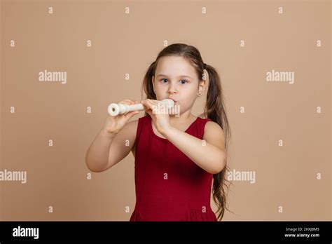 girl in red dress thoughtfully play melody on flute blowing air into duct beige background