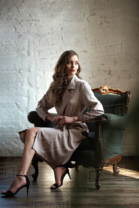 Elegant Woman In Classic Trench Coat Posing In Armchair Stock Photo
