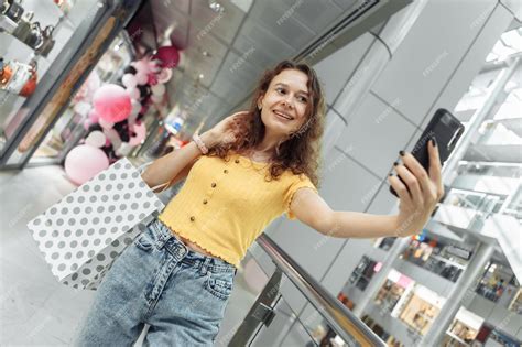premium photo cute woman with curly hair takes a selfie with shopping bags in a shopping