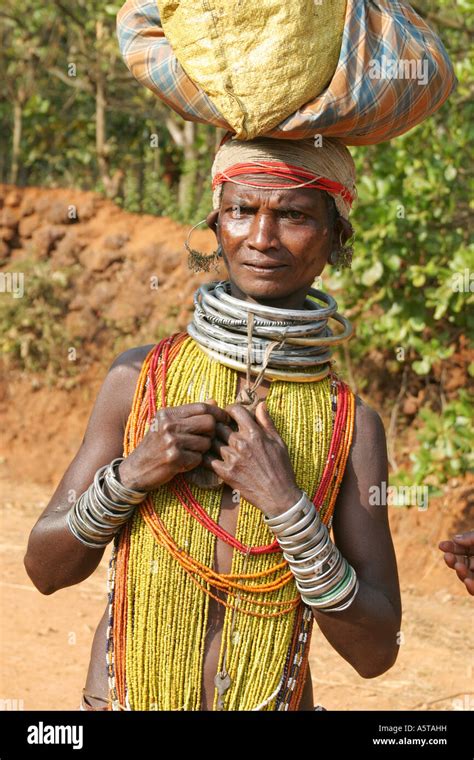bonda tribal woman wearing traditional metal neclets and body beads carrying a heavy load on her