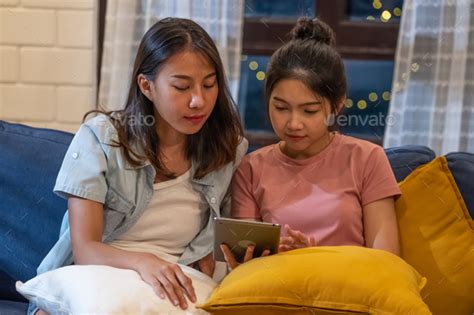 Happy Asian Lesbian Couple Using Tablet Together At Sofa In Living Room