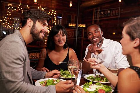 Four Friends Enjoying Dinner And Drinks At A Restaurant Stock Photo
