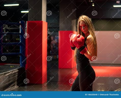 blonde caucasian fighter girl in red boxing gloves is posing in fight club training hall stock