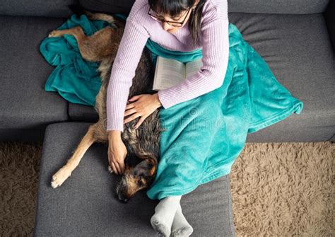 Top View Of Woman Petting Her Crossbreed Dog While Reading A Book On