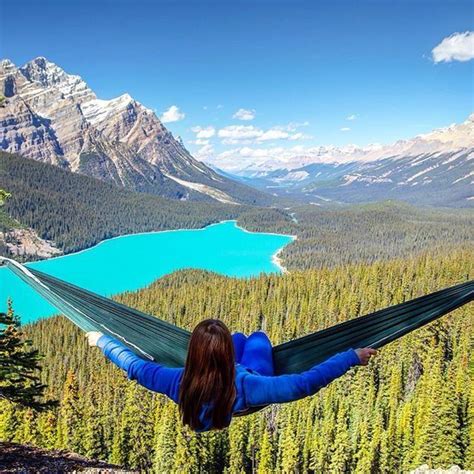 A Woman Laying In A Hammock On Top Of A Mountain Overlooking A Lake