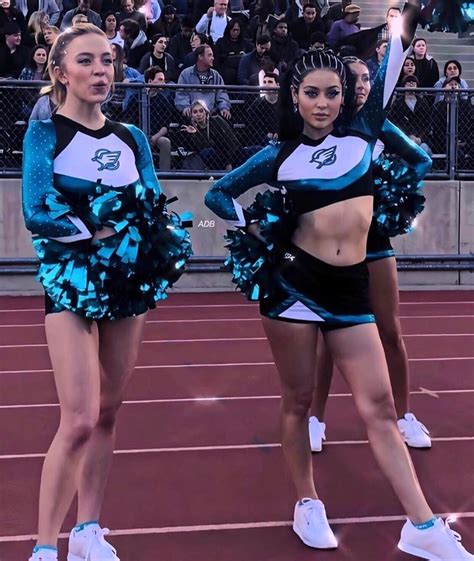 Two Cheerleaders In Blue And Black Outfits Standing On A Track With
