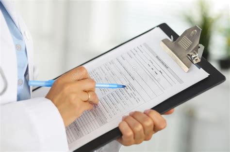 Close Up Of A Female Doctor Filling Up Medical Form At Clipboard While