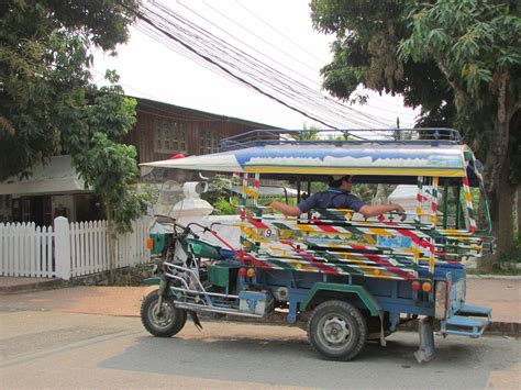 A Colorful Bus Is Parked On The Street In Front Of A White Fence And Trees