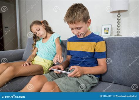smiling siblings using digital tablet on sofa in living room stock image image of domestic