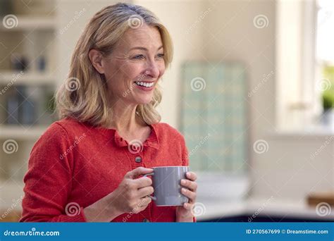 Smiling Mature Woman Standing In Kitchen Relaxing With Cup Of Coffee