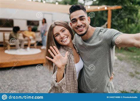 Happy Loving Multiracial Couple Taking Selfie Near Camper Van Resting With Friends Outdoors