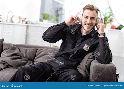 Smiling Police Officer Sitting On Couch And Listening To Music Stock